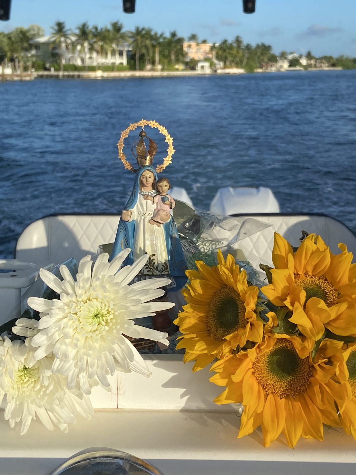 Statue of La Virgen de la Caridad del Cobre with white chrysanthemums and sunflowers on the boat's bow